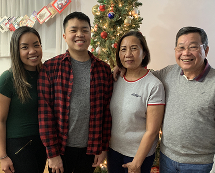 Andy Lam stands and smiles in front of a Christmas tree with his family.