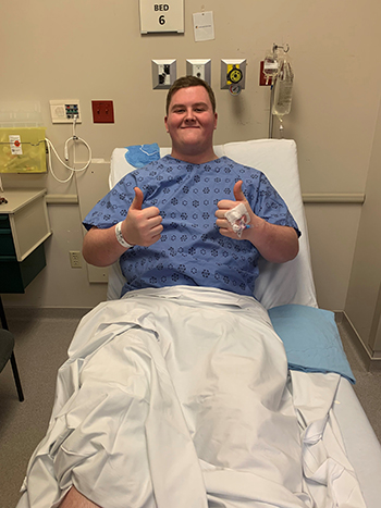 Young man smiling in a hospital bed, giving the thumbs up.