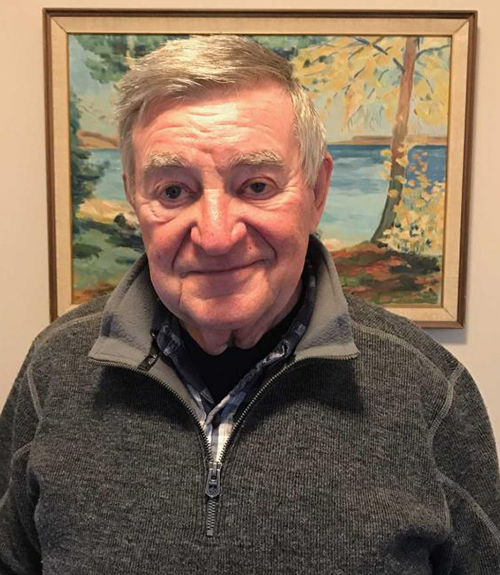 Kind looking male senior standing and smiling in front of a painting.