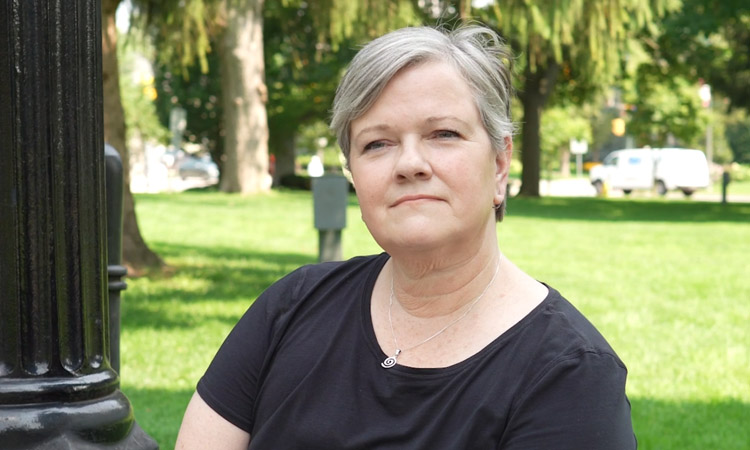 Thoughtful looking woman with short grey hair sitting outside on a sunny day.