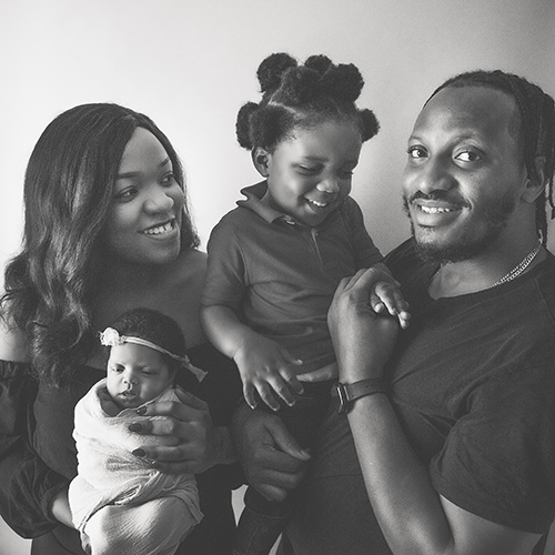Black and white photo of a happy, young family holding their toddler and infant daughter.