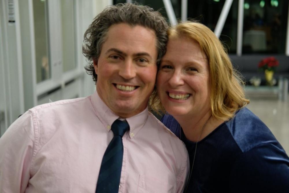 Middle-aged man in collared shirt and tie cheek-to-cheek with his smiling wife.