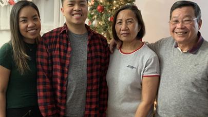 Andy Lam stands and smiles in front of a Christmas tree with his family.