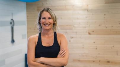Athletic blonde woman in black workout attire, smiling at camera with arms crossed.
