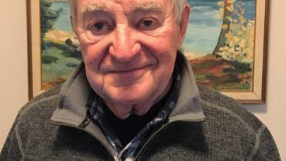 Kind looking male senior standing and smiling in front of a painting.