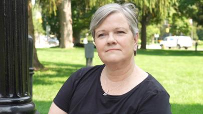 Thoughtful looking woman with short grey hair sitting outside on a sunny day.