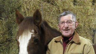 Smiling elderly male standing next to brown horse.