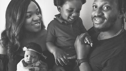 Black and white photo of a happy, young family holding their toddler and infant daughter.