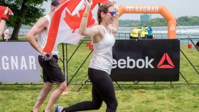 Athletic woman in white shirt running while carrying Canada flag.