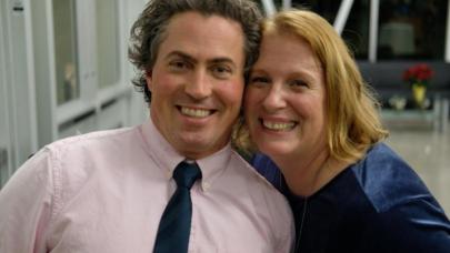 Middle-aged man in collared shirt and tie cheek-to-cheek with his smiling wife.